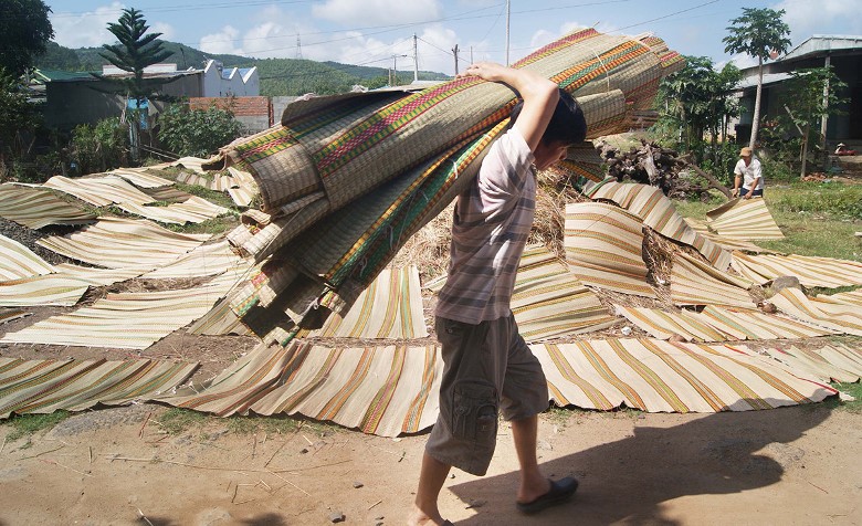 a man is carrying sedge mats to drying place