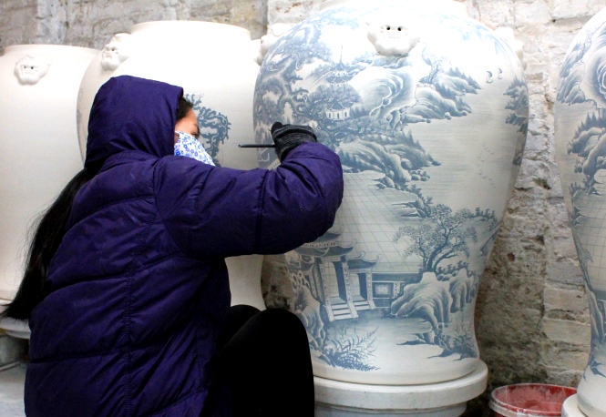 a female artisan is paiting a giant pottery vase