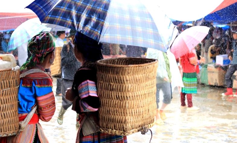 two young women with baskets on their back coming to Bac Ha market on rainy day